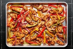 cooked chicken, peppers and onions seasoned with homemade taco seasoning on a baking sheet