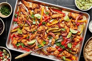 chicken, peppers and onions seasoned with homemade taco seasoning on a baking sheet surrounded by fixings for burrito bowls