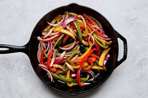 peppers and onions being cooked in a skillet for fajitas