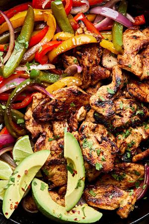 chicken fajitas with peppers and onions in a skillet topped with avocado