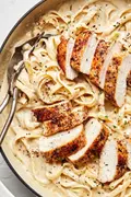 Homemade chicken fettuccine alfredo in a serving bowl with serving spoons