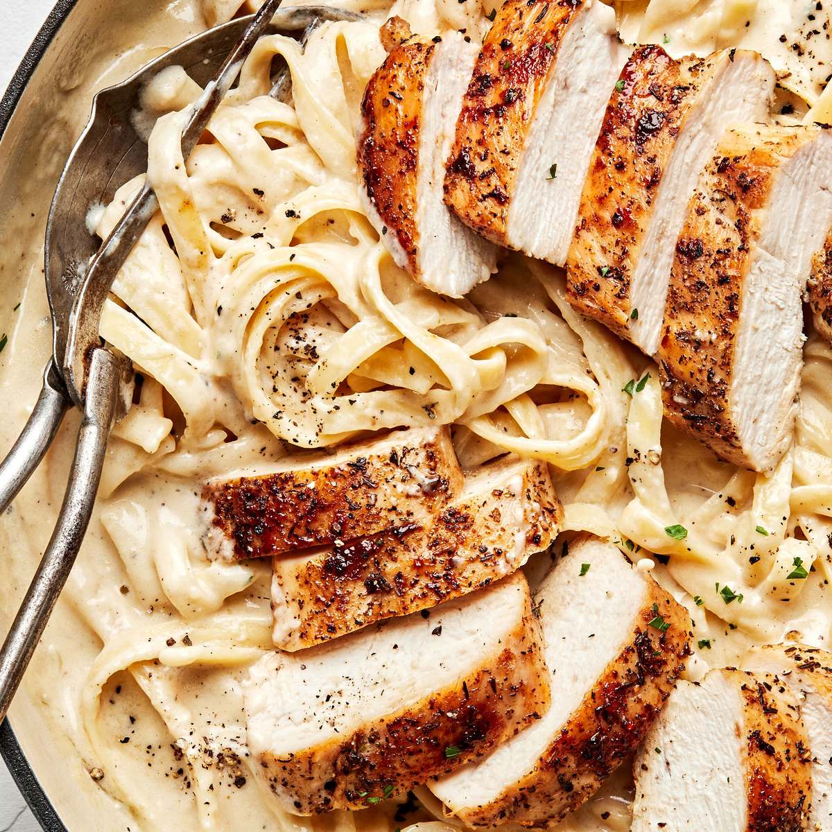 Homemade chicken fettuccine alfredo in a serving bowl with serving spoons