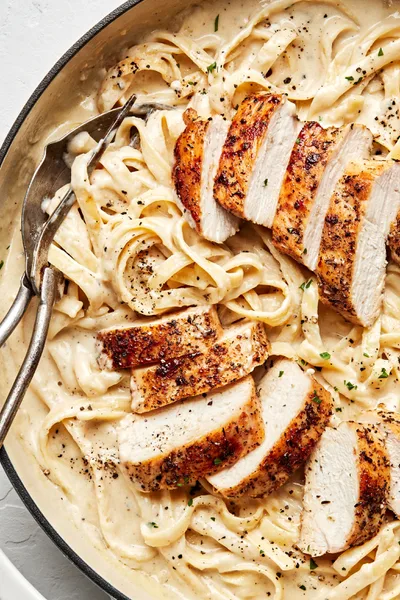 Homemade chicken fettuccine alfredo in a serving bowl with serving spoons