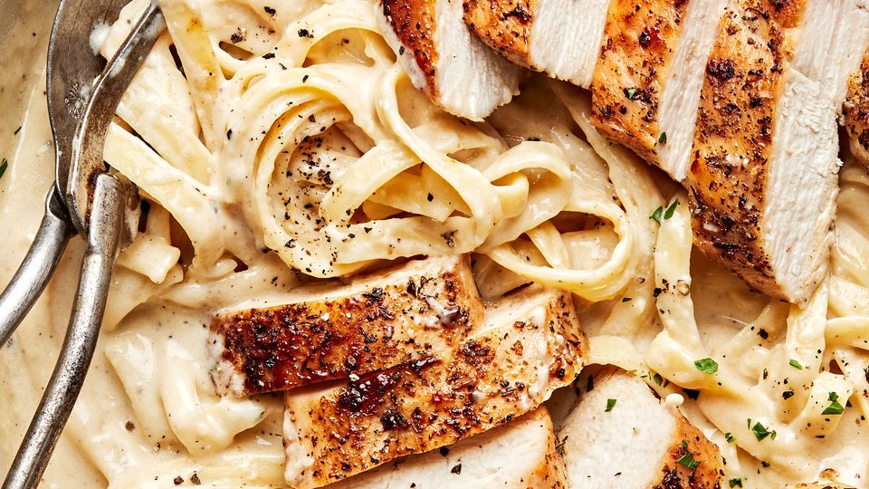 Homemade chicken fettuccine alfredo in a serving bowl with serving spoons
