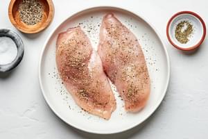 raw chicken being seasoned with salt, pepper and italian seasoning to use for chicken fettuccine alfredo