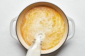 cream being added to a skillet with butter, garlic, garlic powder, nutmeg, salt, and pepper to make homemade alfredo sauce