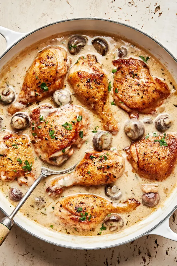 chicken fricassee made with mushrooms, onion, garlic, thyme, bay leaves, nutmeg and sprinkled with parsley in a skillet