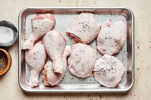 4 skin on chicken legs and 4 bone in chicken thighs seasoned with salt and pepper on a baking sheet