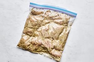 raw chicken thighs marinating in a Greek yogurt marinade in a zip top bag.