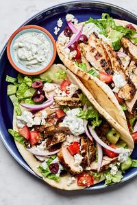 chicken gyros on a plate topped with tzatziki, tomatoes, cucumbers, red onion, greek olives, feta, and romaine