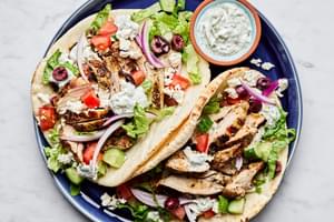 two chicken gyros in pita on a plate surrounded