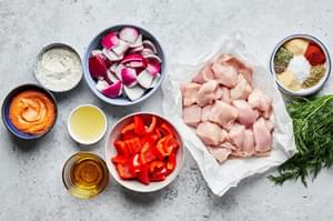 diced raw chicken breast, bell peppers, red onion, spices, olive oil, lemon juice, romesco sauce and dill sauce in prep bowls
