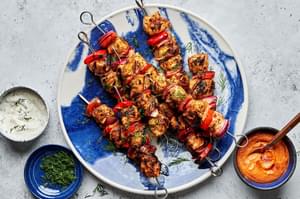 chicken kebabs with bell pepper and red onion on a serving plate served with bowls of dill sauce and romesco sauce