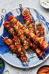 chicken kebabs with bell pepper and red onion on a serving plate served with bowls of dill sauce and romesco sauce