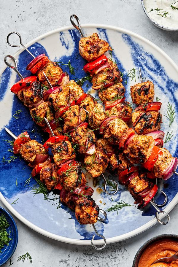 chicken kebabs with bell pepper and red onion on a serving plate served with bowls of dill sauce and romesco sauce