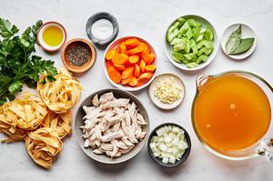onion, celery, carrots, garlic, chicken stock, bay leaves, chicken, egg noodles, salt, parsley and pepper in prep bowls