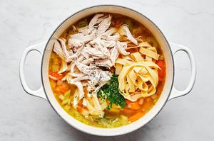 a pot of chicken noodle soup made with onion, celery, carrots, garlic, chicken stock, bay leaves, chicken, egg noodles & salt