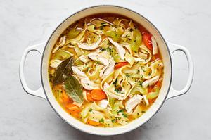 a pot of chicken noodle soup made with onion, celery, carrots, garlic, chicken stock, bay leaves, chicken, egg noodles & salt
