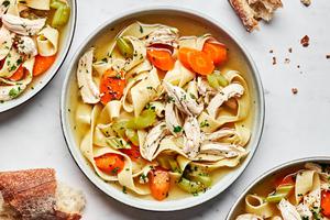 a bowl of homemade chicken noodle soup topped with parsley and pepper served with crusty bread