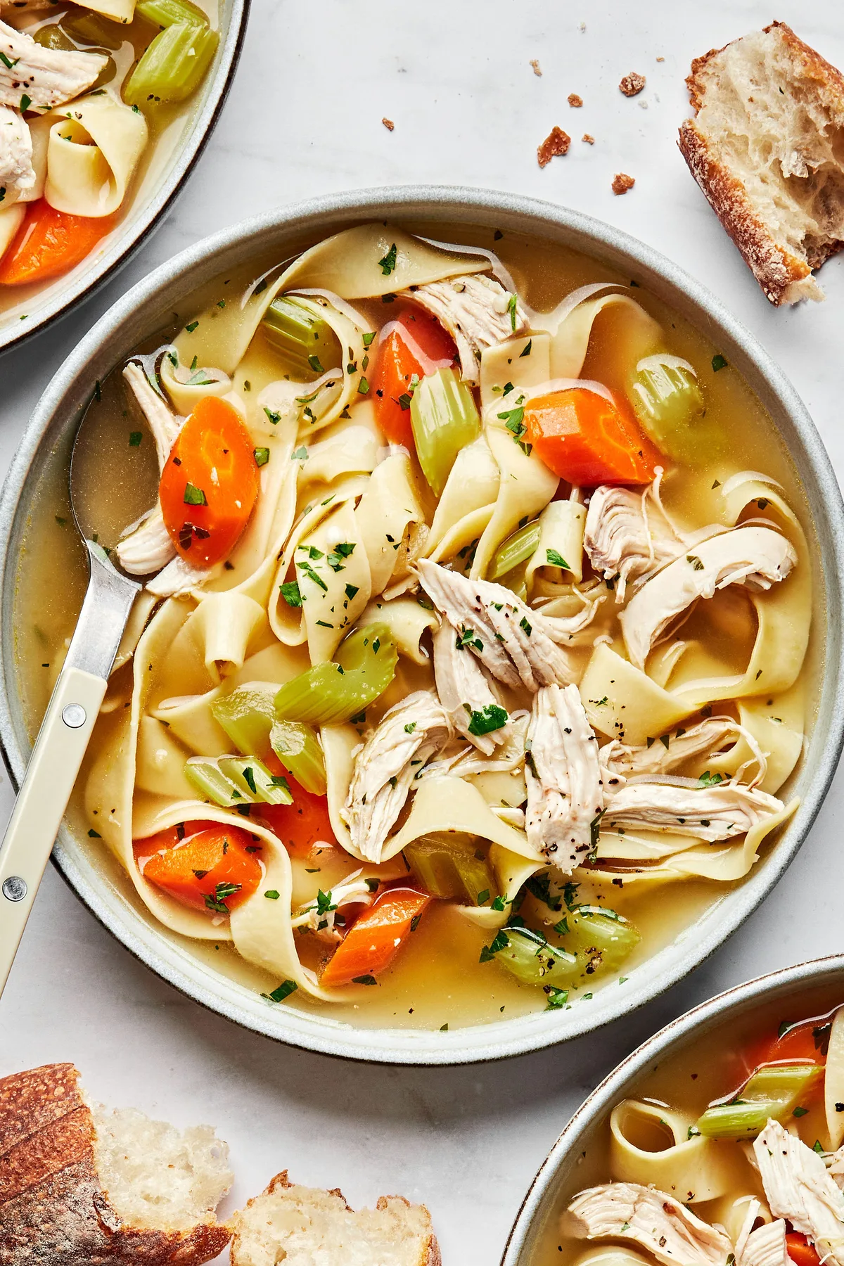 a bowl of homemade chicken noodle soup topped with parsley and pepper served with crusty bread