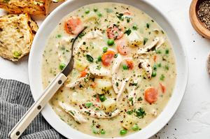 a bowl of homemade chicken pot pie soup sprinkled with pepper in a bowl being served with biscuits.