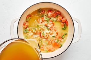 chicken stock being poured into a pot with butter, flour, carrots, celery, and onion