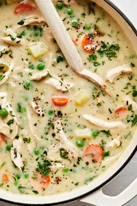 a pot of homemade chicken pot pie soup being stirred with a wooden spoon
