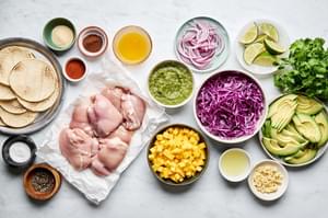 chicken thighs, tortillas, spices, mango, cabbage, avocado, cilantro, limes and salsa verde in prep bowls