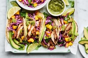 chicken street tacos with mango slaw on corn tortillas, garnished with avocado and lime wedges