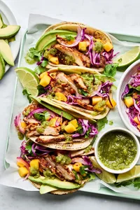 chicken street tacos with mango slaw being on corn tortillas, garnished with avocado and lime wedges