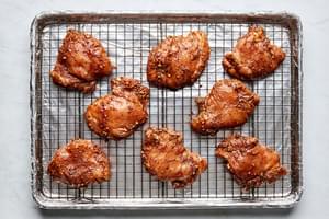 marinated chicken thighs on a rack inside a foil lined baking sheet