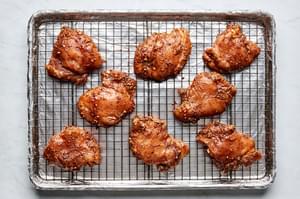 marinated chicken thighs on a rack inside a foil lined baking sheet