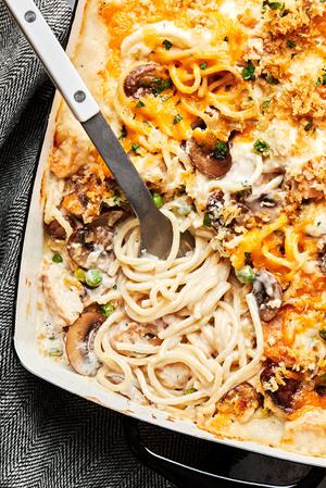 chicken tetrazzini being scooped out of a baking dish made with, mushrooms, peas, cream sauce, cheddar, Parm and panko