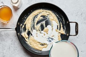 milk and cream being poured into a skillet with a butter and flour rue