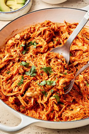 A pot filled with smoky chicken tinga, featuring shredded chicken simmered in a rich tomato and chipotle sauce