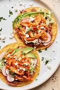 2 chicken tinga tacos served on corn tortillas topped with shredded cabbage, radishes, cotija and sliced avocado