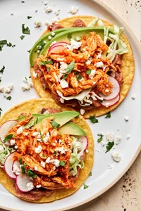 2 chicken tinga tacos served on corn tortillas topped with shredded cabbage, radishes, cotija and sliced avocado