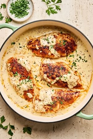 Chicken breasts in a skillet, smothered in a creamy mustard sauce and garnished with parsley.