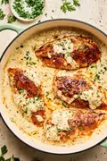 Chicken breasts in a skillet, smothered in a creamy mustard sauce and garnished with parsley.