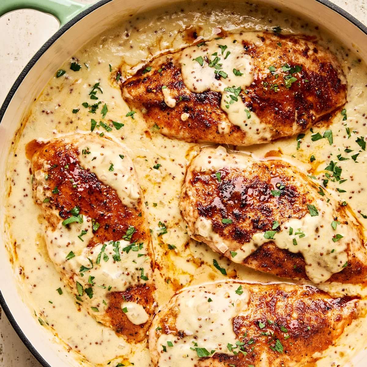 Chicken breasts in a skillet, smothered in a creamy mustard sauce and garnished with parsley.