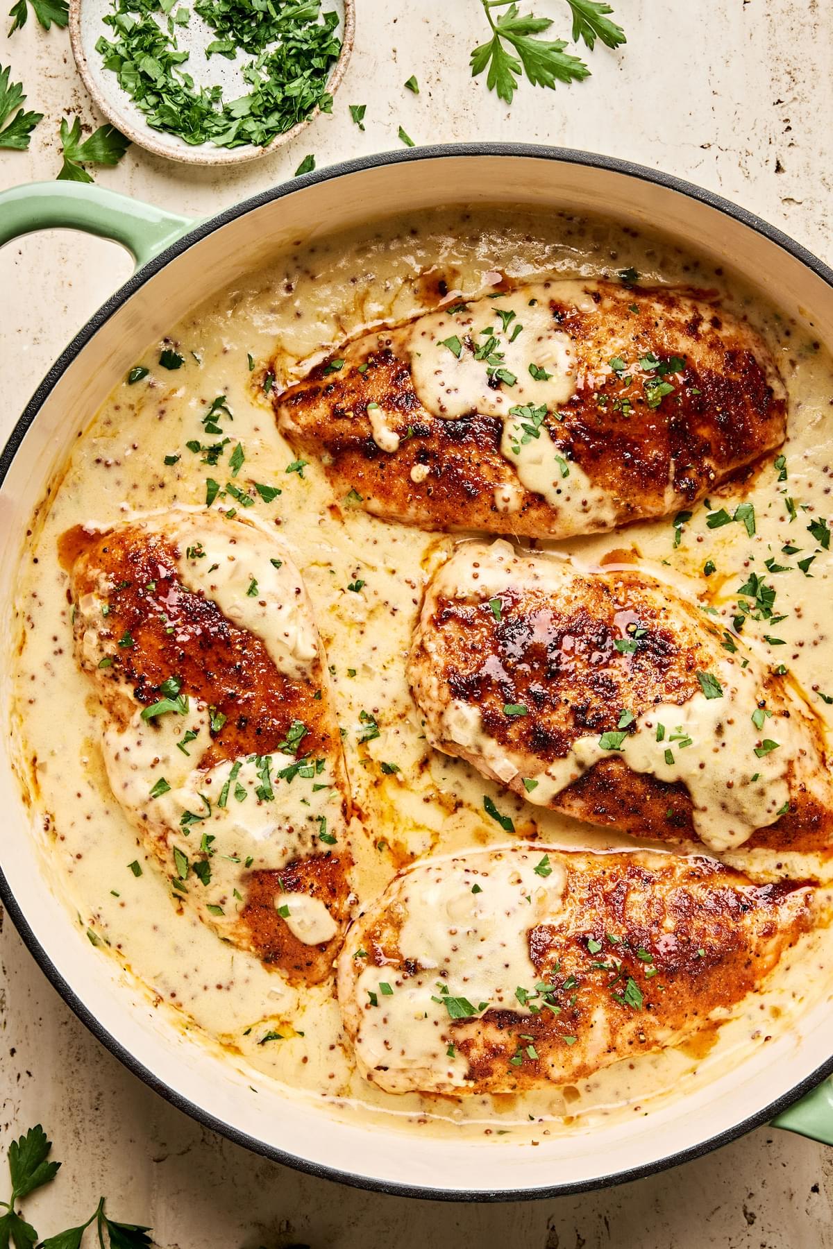 Chicken breasts in a skillet, smothered in a creamy mustard sauce and garnished with parsley.