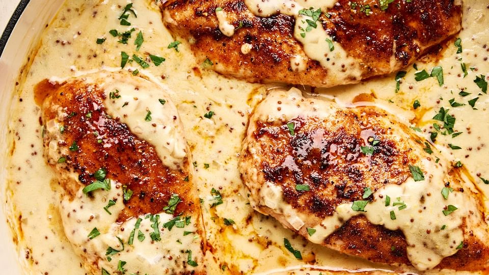 Chicken breasts in a skillet, smothered in a creamy mustard sauce and garnished with parsley.
