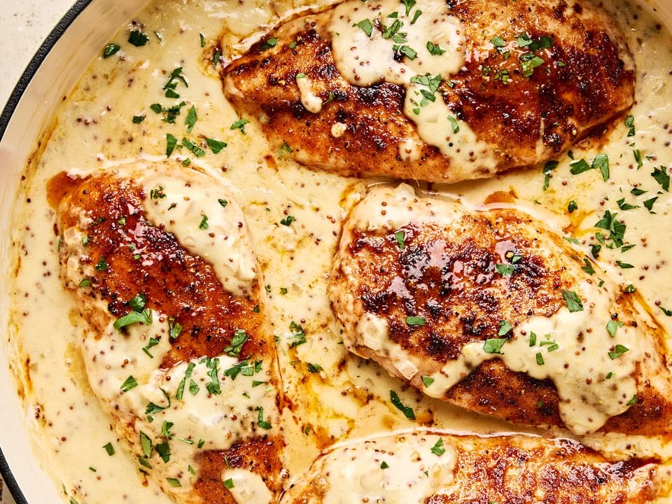 Chicken breasts in a skillet, smothered in a creamy mustard sauce and garnished with parsley.