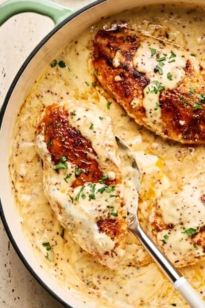 Chicken breasts in a skillet, smothered in a creamy mustard sauce and garnished with parsley.