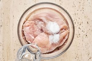 raw chicken added in a bowl with water and salt to soak in a wet brine before baking