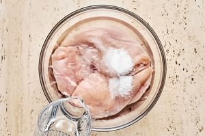 raw chicken added in a bowl with water and salt to soak in a wet brine before baking
