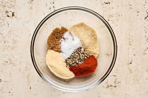 A bowl of assorted spices being mixed together to make a dry rub for seasoning chicken