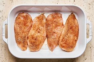 Brined chicken breasts coated in a colorful spice rub in a baking dish, ready for baking.