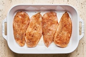 Brined chicken breasts coated in a colorful spice rub in a baking dish, ready for baking.