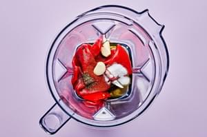 roasted red peppers, garlic, paprika, cayenne, salt, olive oil, thyme & honey being added to a blender.